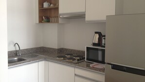A kitchen with white cabinets, a stainless steel sink, a microwave, and a kettle on the countertop. - Nice 1- Bedroom Condo In Klong Muang (Klong Muang)