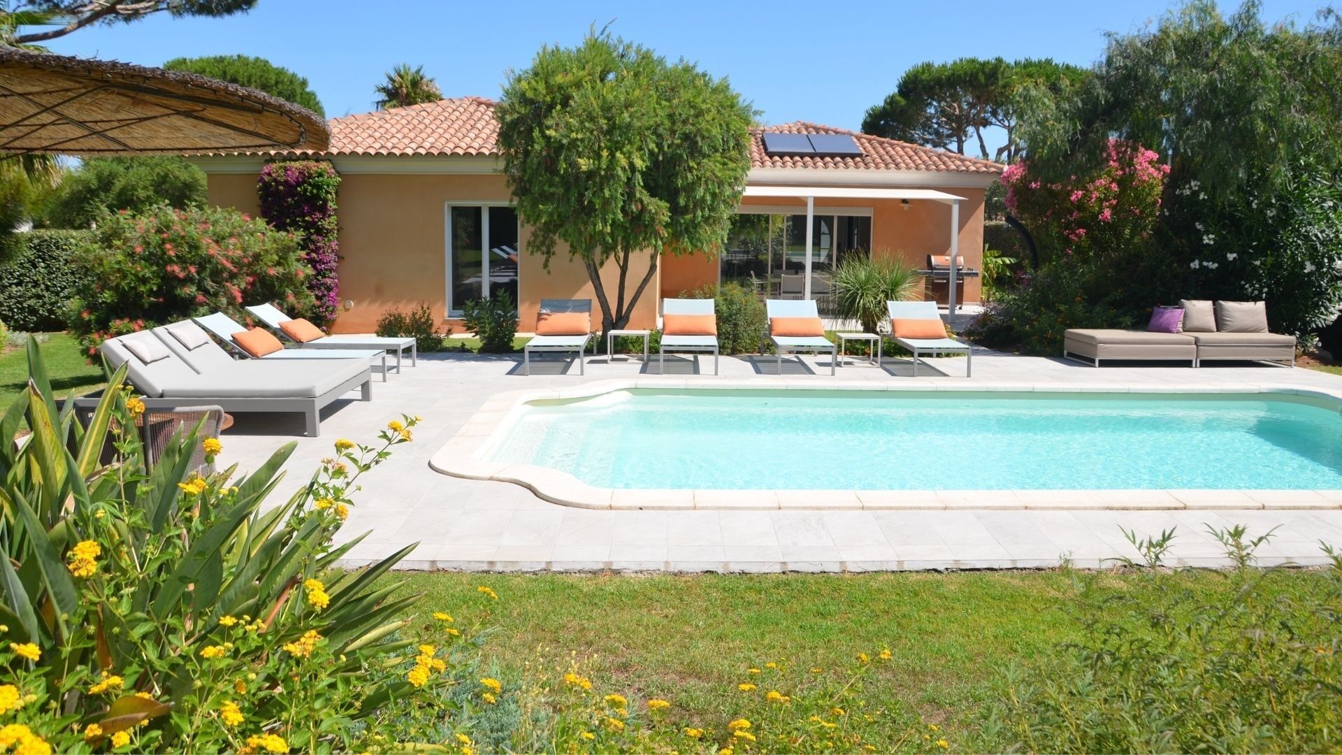 A poolside area with lounge chairs, a pool, and a building with a tiled roof.