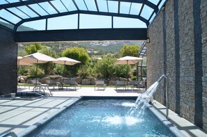 An outdoor swimming pool with a water feature, surrounded by lounge chairs and umbrellas, with a view of a mountainous landscape. - Master Suite Villa featuring a Private Pool, Garden, Parking and Spa (CALVI)