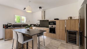 A modern kitchen with a central island, wooden cabinets, stainless steel appliances, and a window providing natural light.