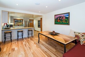 Une cuisine moderne avec un plancher en bois, des tabourets de bar, une table à manger et un tableau accroché au mur.