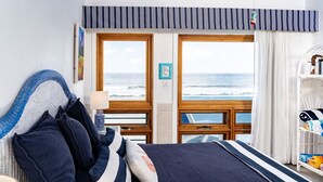 A bedroom with a large bed, a view of the ocean, a striped curtain, and a bookshelf.