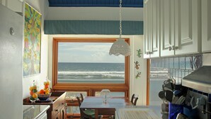 A kitchen with a view of the ocean, a dining table, and a hanging light fixture.