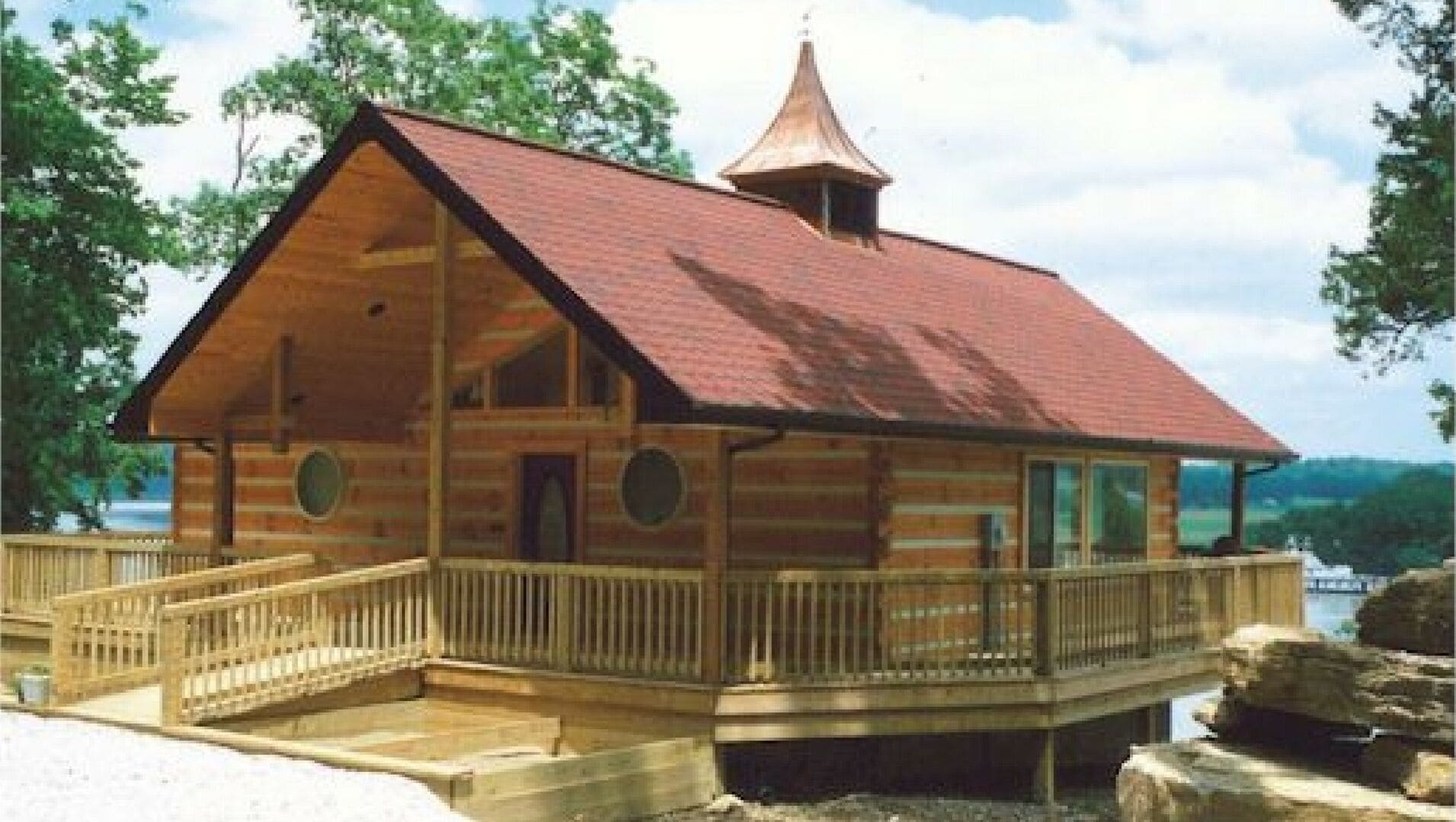 Una cabaña de madera con techo rojo, un balcón y una pequeña estructura similar a una torre en el techo.