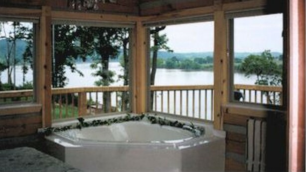 Eine Holzhütte mit Whirlpool, großen Fenstern und Seeblick.