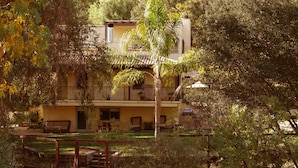 A two-story building with a balcony, surrounded by lush greenery and trees.