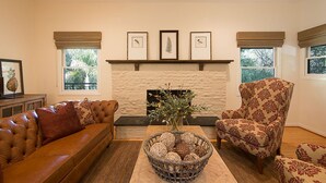 A living room with a fireplace, two sofas, a patterned armchair, and a basket of decorative balls.