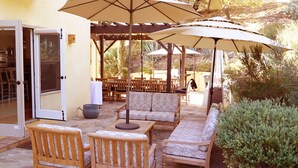 An outdoor patio with wooden furniture, including sofas and chairs, under large umbrellas.