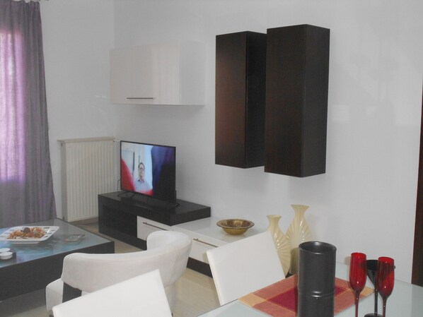 A modern living room with a flat-screen TV, white furniture, and decorative items. - *Paradise City* Apartment in the center of Rethymno, near the sea (Ρέθυμνο)