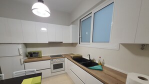 A compact kitchen with white cabinets, a built-in oven, a sink, and a window above the sink.