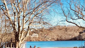 A lakeside view with a large tree, a small dock, and a building in the background. - Charming 18th century cottage with its own beachfront on Scargo Lake near bay (Dennis)
