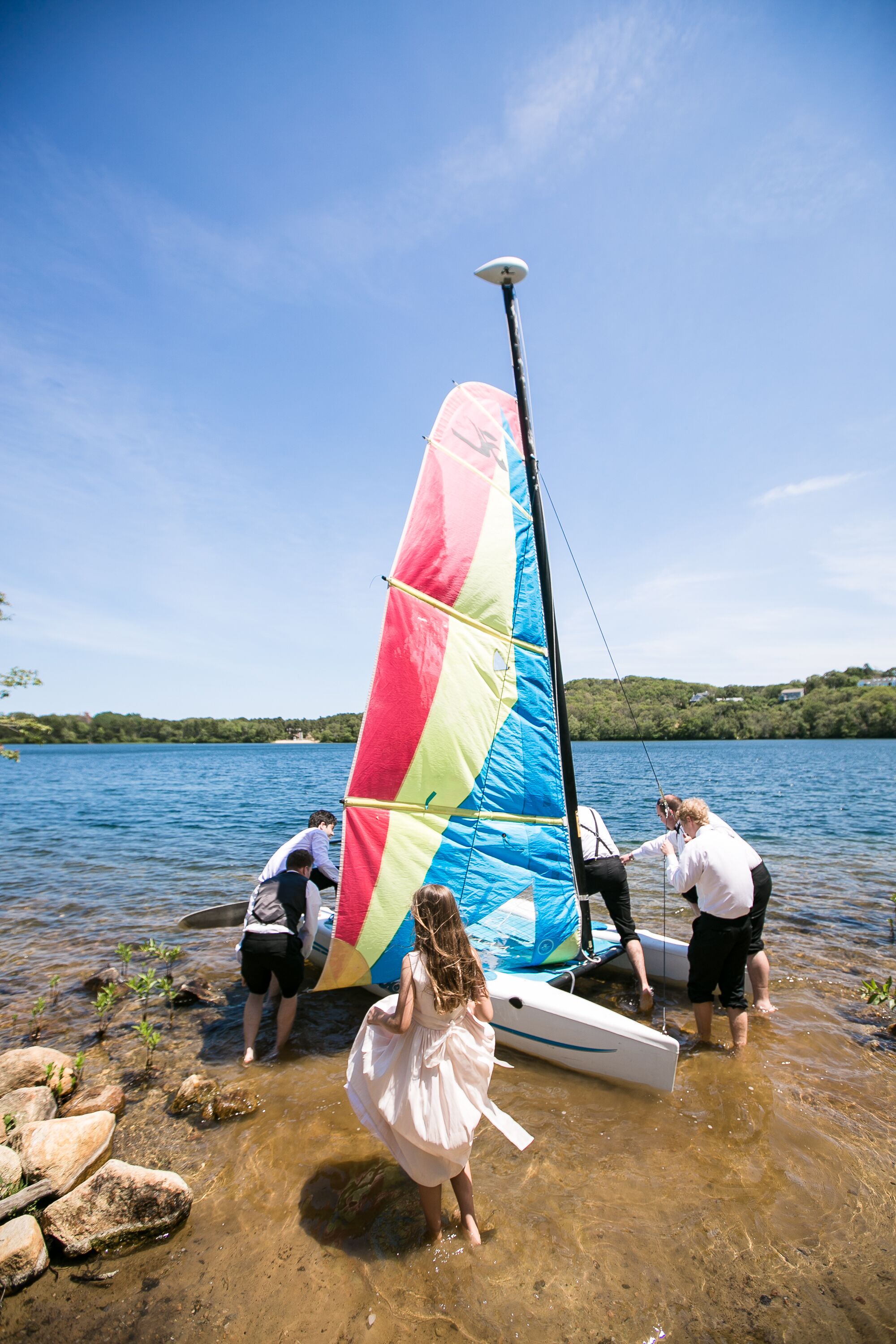 Un velero con vela colorida amarrado a la orilla de un lago.