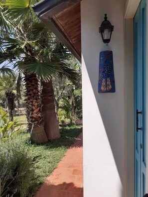 Un camino que lleva a un edificio con una puerta azul, un farol en la pared y una palmera.