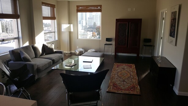 Un salon moderne avec un canapé, une table basse en verre, un lampadaire, un fauteuil, un tapis et une vue sur la ville à travers de grandes fenêtres.