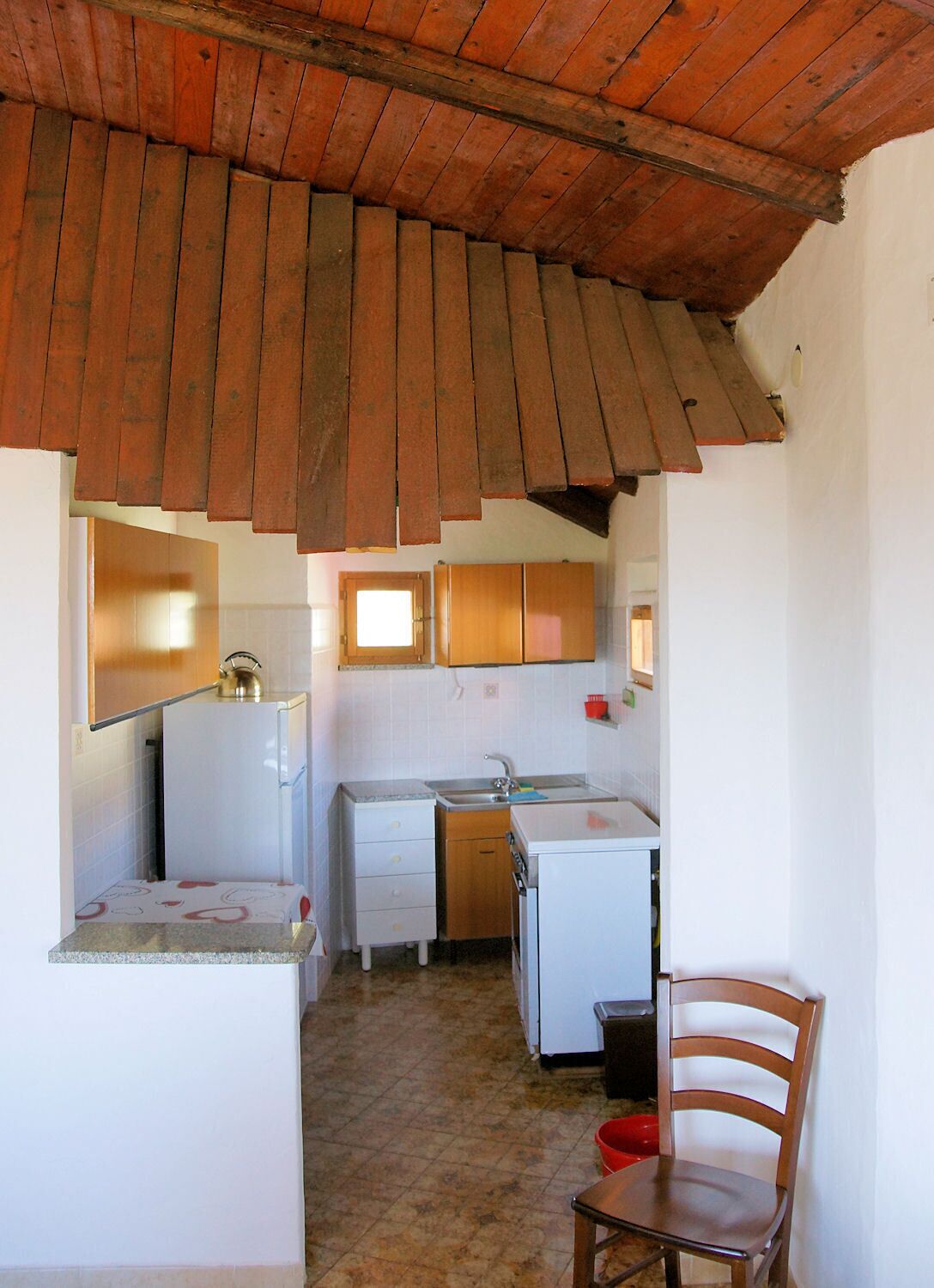 Una cuina compacta amb armaris de fusta, un frigorífic blanc i un rentaplat.