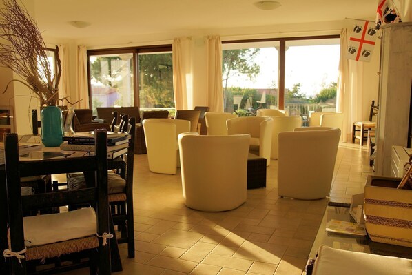 A spacious living room with a large window, a dining area with a table and chairs, and a view of greenery outside.