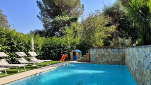 Una piscina con sillones de descanso, un tobogán y un muro de piedra.