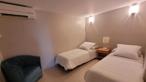 Una habitación pequeña y limpia con dos camas, una silla y una mesita de noche.