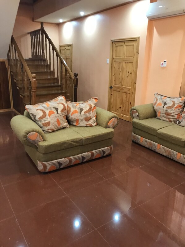 A hallway with two green sofas with patterned cushions, a wooden staircase, and a wooden door.