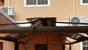 Uma área externa coberta com teto de metal, guarda-corpo branco e porta que dá para um espaço interno.