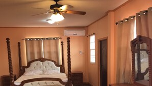 Quarto com cama de dossel, penteadeira de madeira, uma cadeira e um ventilador de teto.