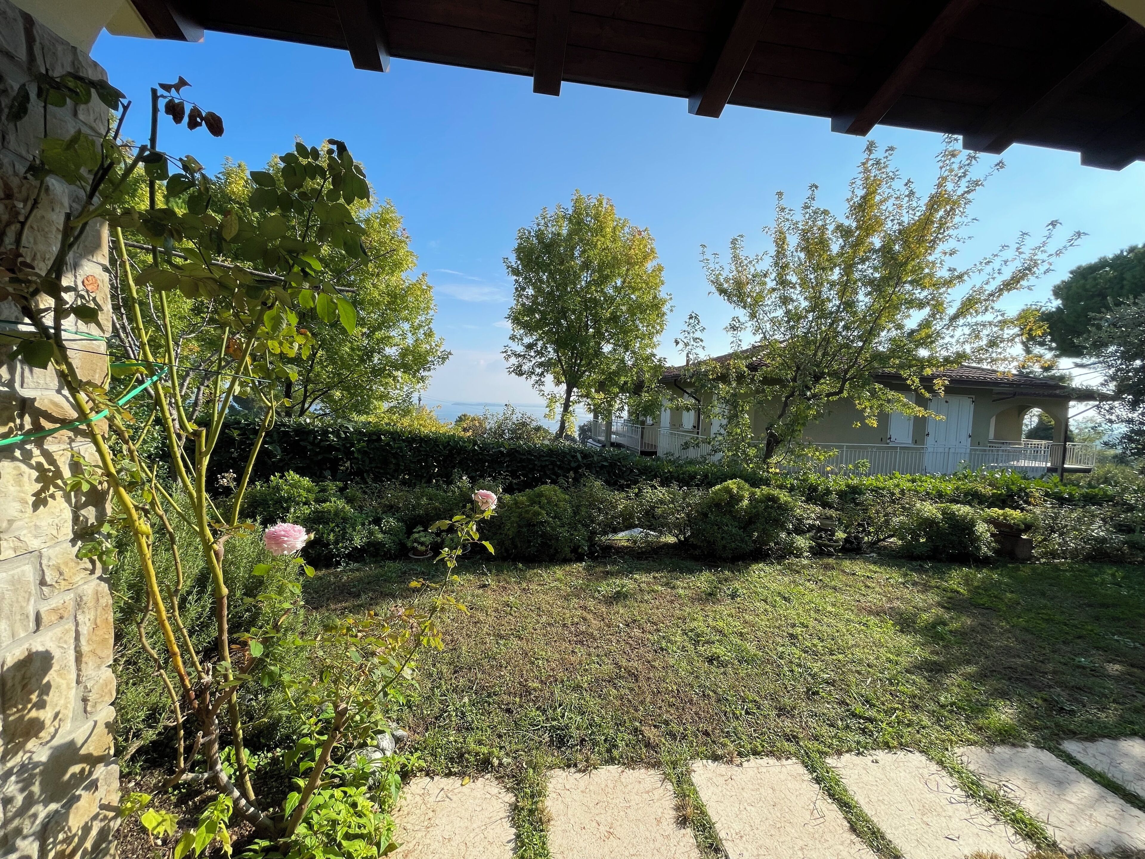 Ein Garten mit einer Steinmauer, einer Pergola und Blick auf ein Haus mit Balkon.