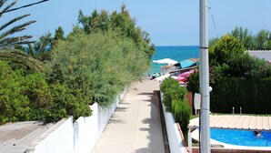 A pathway leading to a beach with a pool and umbrellas. - 121 Las Velas (Denia)