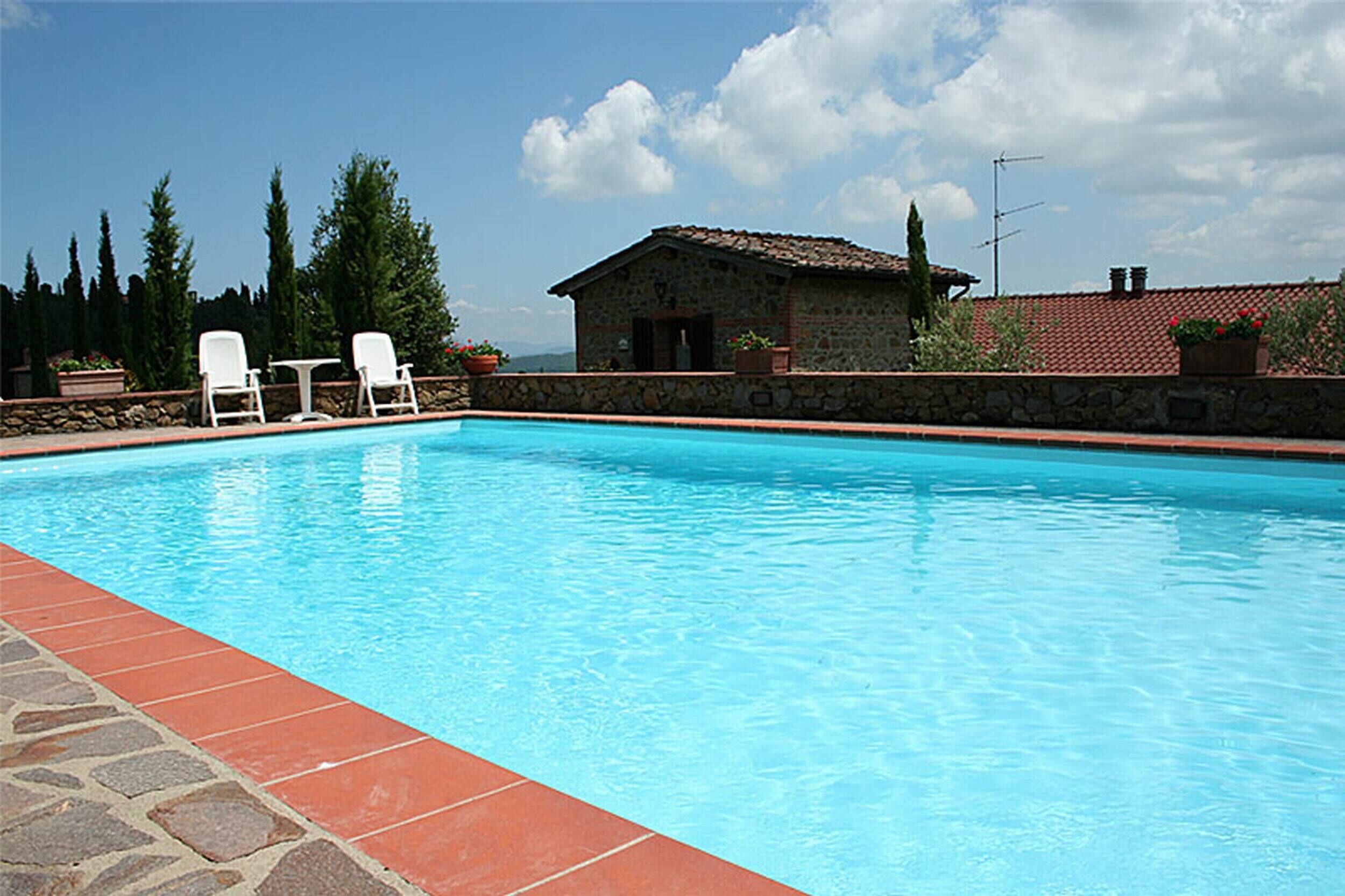 Una piscina azul cristalina con sillas de descanso blancas y un edificio de piedra al fondo.