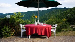 Een tafel met een rode tafelkleed, twee witte stoelen, een groene parasol, een vaas met bloemen en een fles wijn.