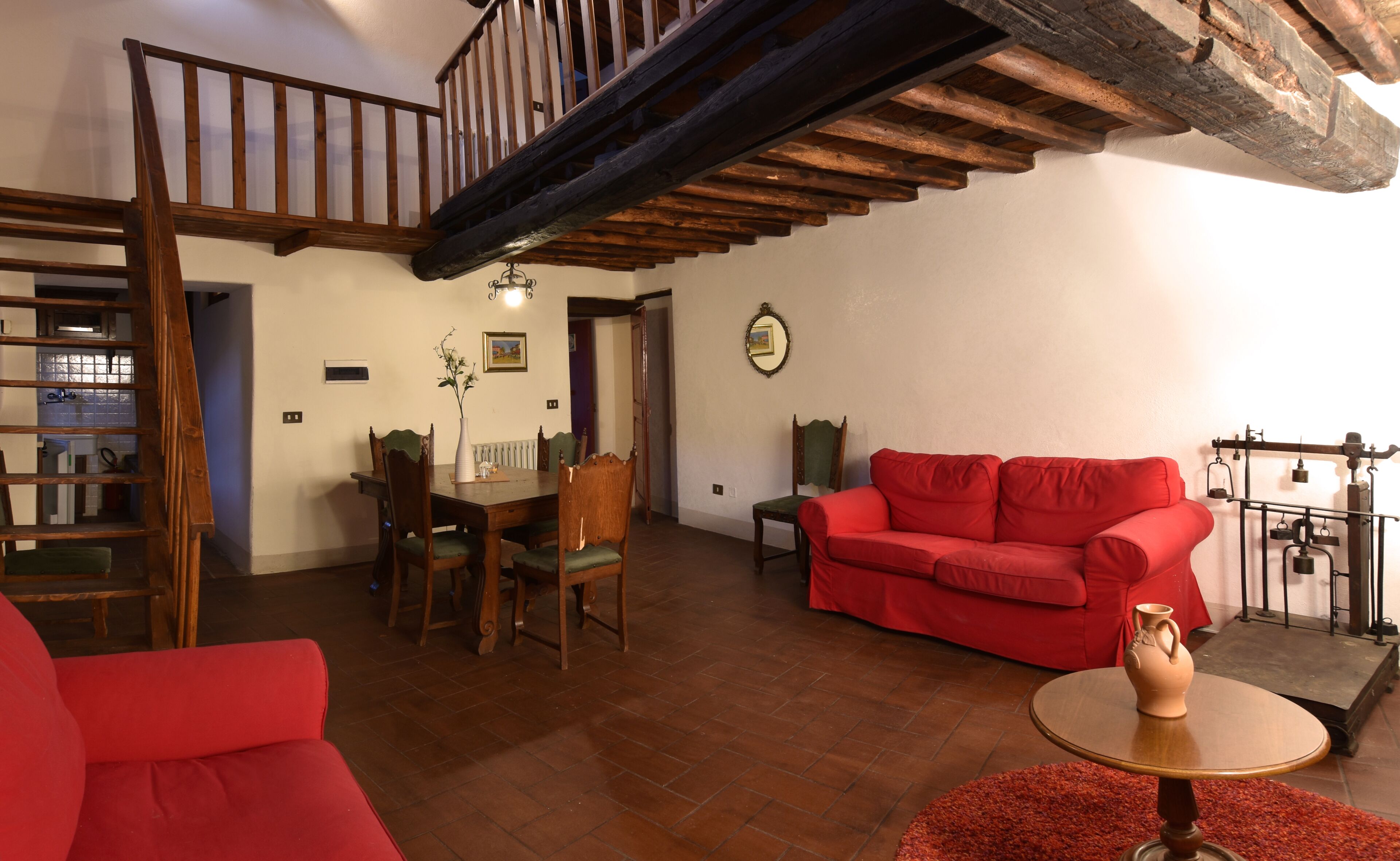 Un grand salon avec un canapé rouge, une table à manger et des chaises, un escalier et un tapis rouge.
