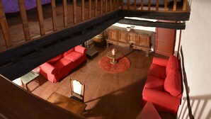 Ruime loft slaapkamer met een hoge plafond, een houten trap, een rode zithoek, een klein rond tafeltje en een decoratieve vaas.