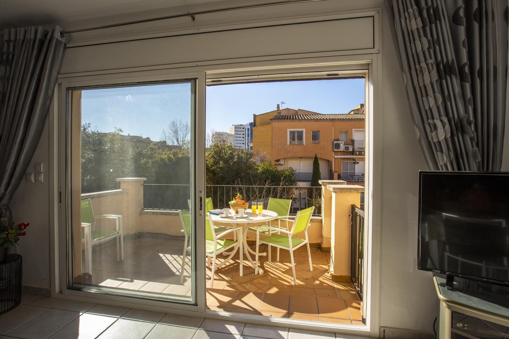 A balcony with a table and chairs, a TV, and a view of buildings and trees.