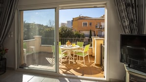 Ein Balkon mit Tisch und Stühlen, einem Fernseher und Blick auf Gebäude und Bäume.
