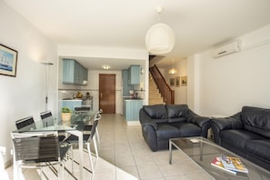Een moderne woonkamer met een glazen eettafel, een zwarte leren bank en een trap die naar een keuken leidt.