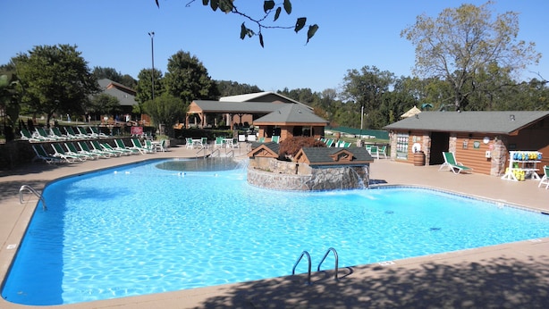 A swimming pool with a small waterfall feature, surrounded by lounge chairs and shaded areas.