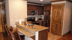 A kitchen with granite countertops, stainless steel appliances, wooden cabinets, and a wooden door.