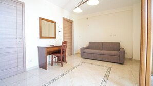 Une pièce comprenant un bureau en bois, une chaise, un canapé, un miroir et un luminaire fixé au plafond.