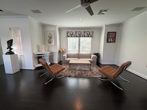 A living room with a dark wooden floor, a white sofa, two brown chairs, a coffee table, and a ceiling fan.