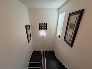 A narrow stairway with dark wooden steps, white walls, and framed artwork on the walls.
