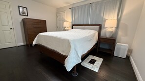 Una camera da letto con un letto in legno, una cassettiera, un comodino con una lampada, un termosifone e un tappeto.