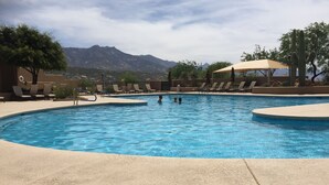 Uma piscina com espreguiçadeiras e guarda-sóis, cercada por árvores e montanhas ao fundo.