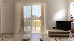 A modern living room with a large sliding glass door leading to a balcony, a flat-screen TV, a remote control, and a small potted plant. - 110 Alberca 7-6 (Denia)