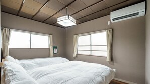 A hotel room with two beds, large windows, an air conditioning unit, and a hanging light fixture.