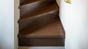 A wooden staircase with a handrail, a light switch, and an exit sign on the wall.
