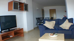 A living room with a television on a wooden stand, a blue sofa with two pillows, and a small table with a bowl of snacks. - FRENTE AL MAR, WIFI, 130M2 (Empuriabrava)