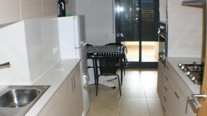 A compact kitchen with a sink, stove, and a small dining area with a chair. - FRENTE AL MAR, WIFI, 130M2 (Empuriabrava)