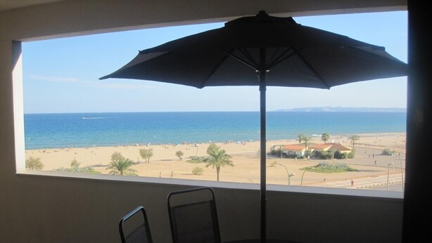 A room with a large window overlooking a beach, a table with chairs, and a floor lamp. - FRENTE AL MAR, WIFI, 130M2 (Empuriabrava)