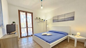A bedroom with a bed, a TV, a desk, a lamp, and a painting on the wall.