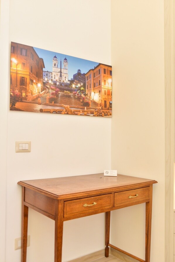 A room with a wooden desk, a framed picture of a cityscape, and a light switch on the wall.