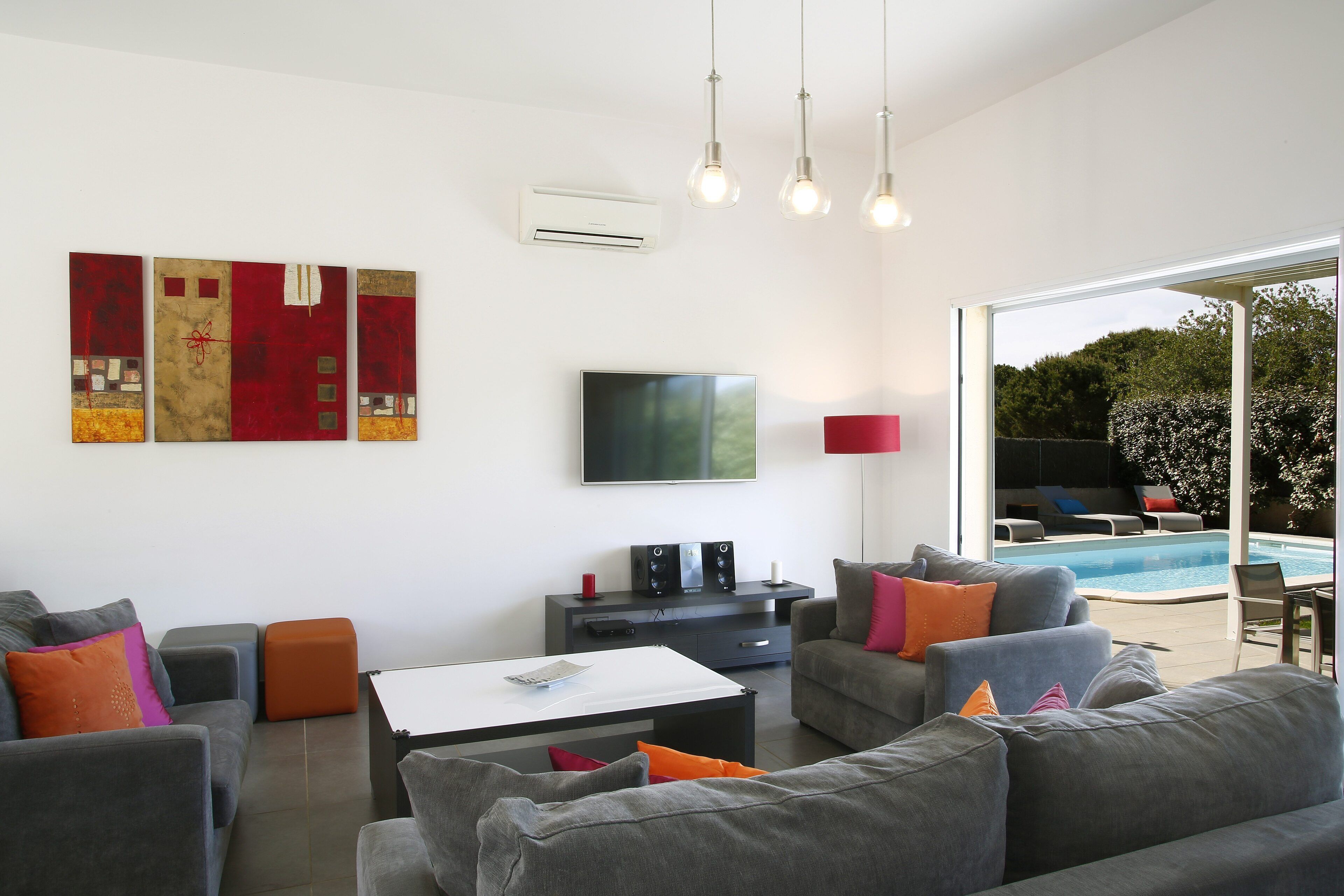 A modern living room with grey sofas, a coffee table, a flat-screen TV, and a pool outside.